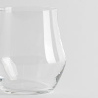 Transparentes Glas mit dicker Basis und leicht gebogenen Wänden auf einheitlichem weißem Hintergrund