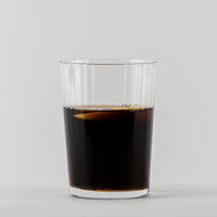 Transparant geribbeld glas met donkere vloeistof op lichtgrijze achtergrond