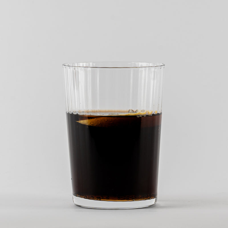 Transparant geribbeld glas met donkere vloeistof op lichtgrijze achtergrond