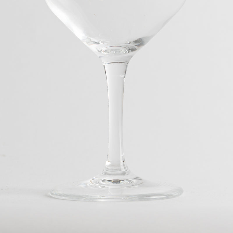 Transparent glass wine glass with thin stem and round base on neutral white background