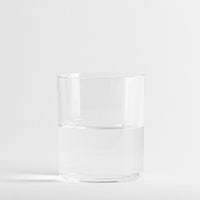 Verre transparent en verre à moitié rempli d'eau, sur fond blanc uniforme.