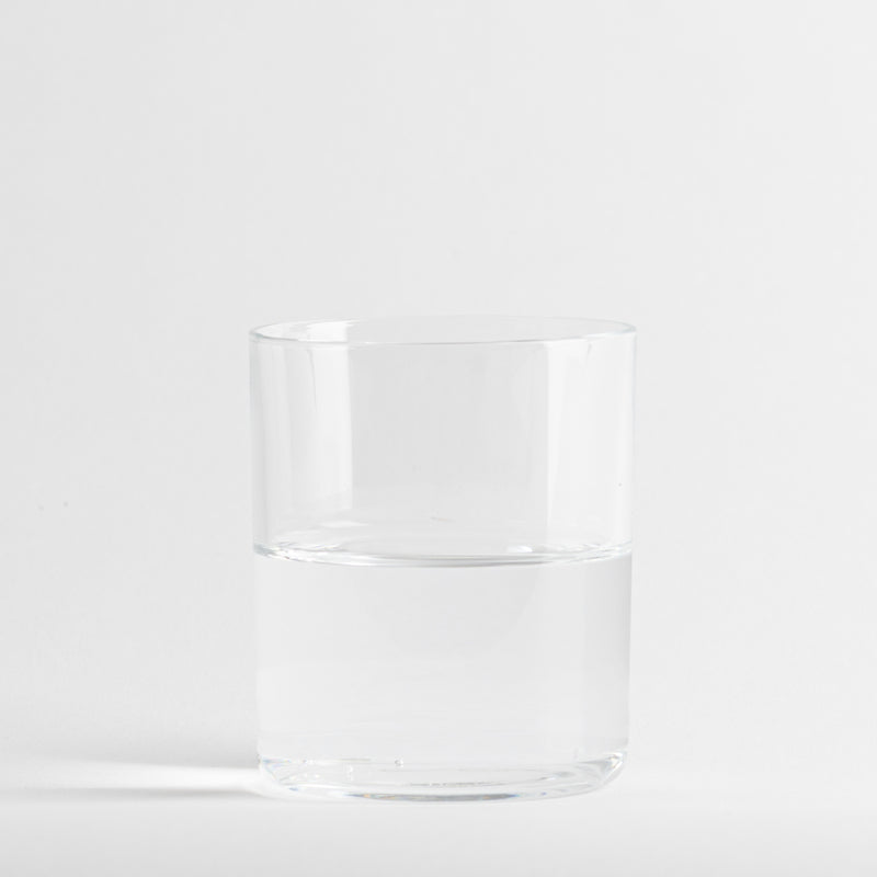 Verre transparent en verre à moitié rempli d'eau, sur fond blanc uniforme.