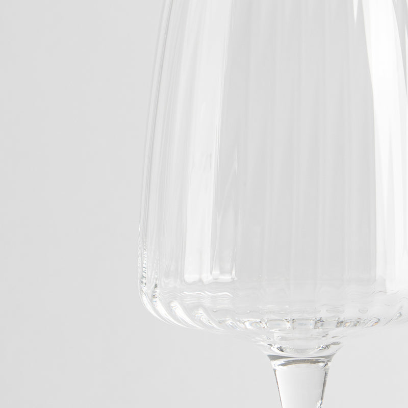 Transparent glass wine glass with ribbed surface on neutral white background.