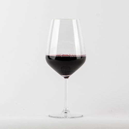 bicchiere di vetro trasparente a stelo con vino rosso scuro su sfondo bianco