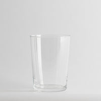 Vaso transparente de cristal con forma cilíndrica, sobre fondo gris claro uniforme