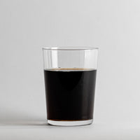 Vaso transparente de forma cilíndrica de cristal que contiene líquido oscuro sobre fondo blanco.