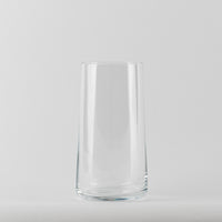 Vaso transparente de cristal con forma cilíndrica ligeramente cónica sobre fondo blanco uniforme.