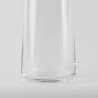 Vaso de vidrio transparentee, forma cilíndrica csobre flat base, resting sobre superficie bianca.