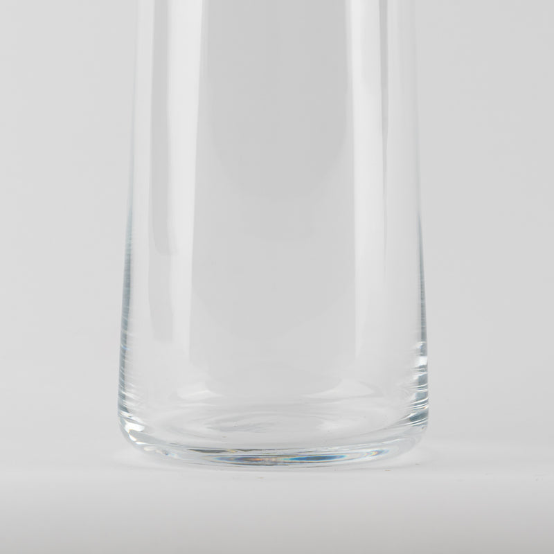Vaso de vidrio transparentee, forma cilíndrica csobre flat base, resting sobre superficie bianca.