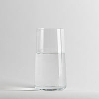 Vaso transparente cilíndrico de cristal con agua limpia en el interior, fondo gris claro