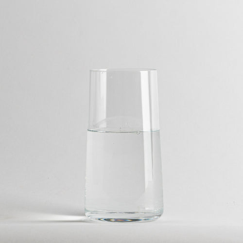 Bicchiere trasparente cilindrico in vetro con acqua limpida all'interno, sfondo grigio chiaro