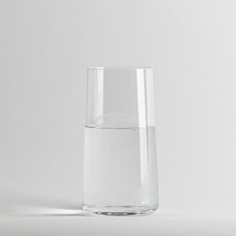 Vaso transparente cilíndrico de cristal con agua limpia en el interior, fondo gris claro