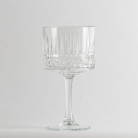Vaso transparente de vidrio con tallo alto y decoraciones geométricas en el cuerpo, fondo gris claro