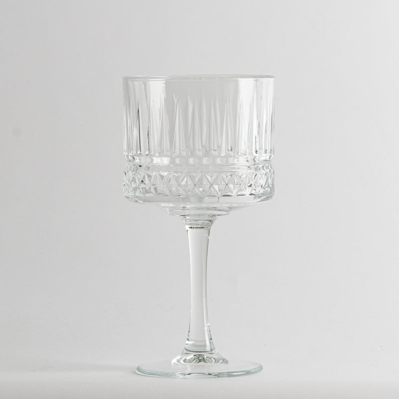 Vaso transparente de vidrio con tallo alto y decoraciones geométricas en el cuerpo, fondo gris claro