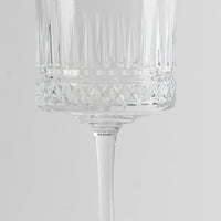 Copa de vidrio transparente con decoraciones geométricas y tallo fino sobre fondo gris claro