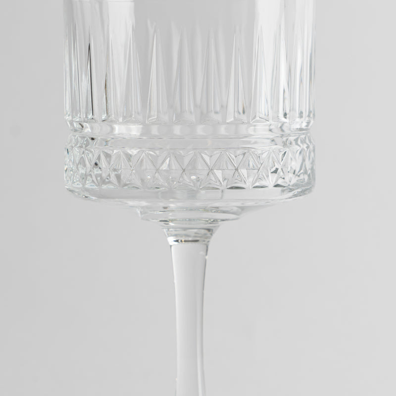 Copa de vidrio transparente con decoraciones geométricas y tallo fino sobre fondo gris claro