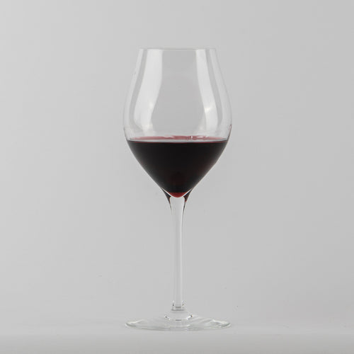 transparante glazen beker met vino rood op uniform lichtgrijze achtergropd