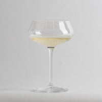 Calice en verre transparent à coupe avec vin blanc pétillant sur fond gris clair.