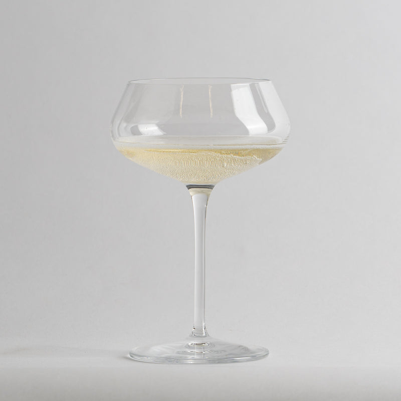 Calice en verre transparent à coupe avec vin blanc pétillant sur fond gris clair.