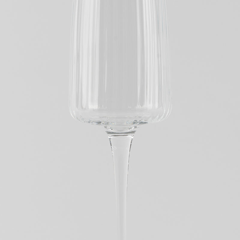 Verre à vin en verre transparent à structure à rainures verticales sur fond gris clair.