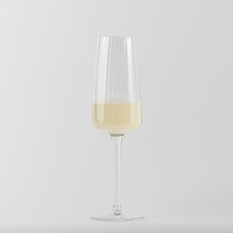 Verre à vin en verre transparent avec liquide jaune clair et bulles sur fond gris clair