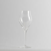 Transparent glass with sinuous shape and thin stem on light grey background