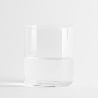 Transparentes zylindrisches Glas halb gefüllt mit klarem Wasser auf weißem Hintergrund.