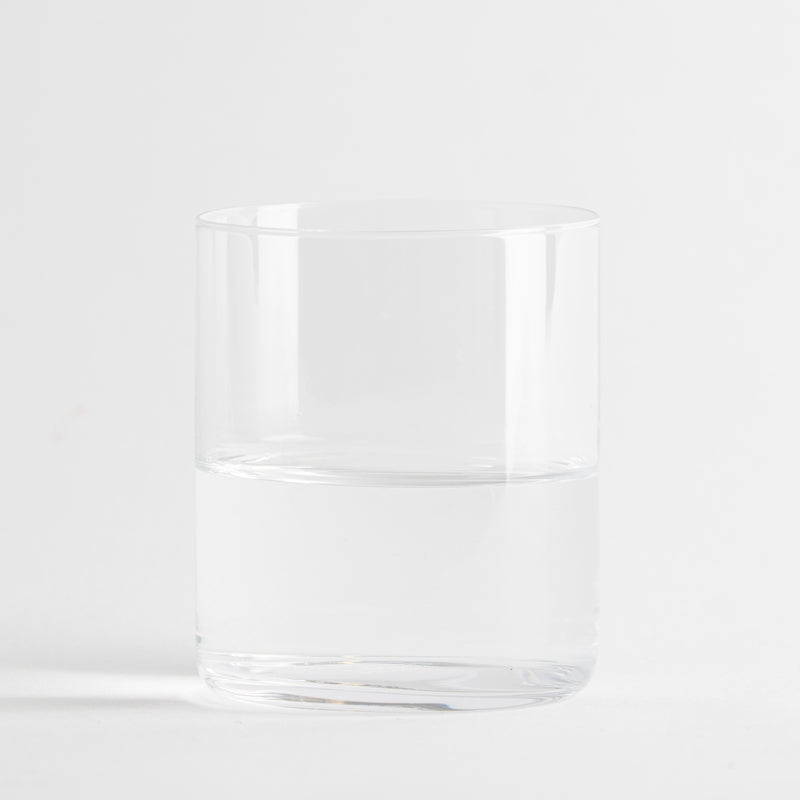 Transparentes zylindrisches Glas halb gefüllt mit klarem Wasser auf weißem Hintergrund.