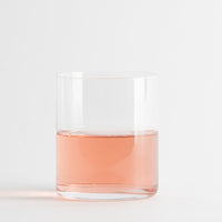 Transparentes zylindrisches Glas mit rosa Flüssigkeit auf neutralem weißem Hintergrund