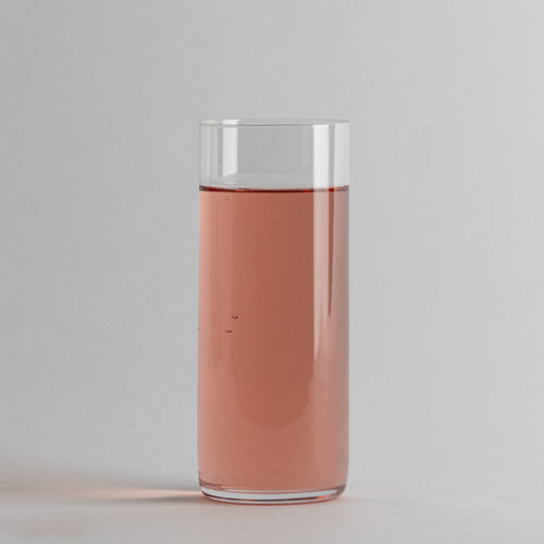 Bicchiere cilindrico trasparente con liquido rosa, sfondo grigio uniforme, superficie liscia.