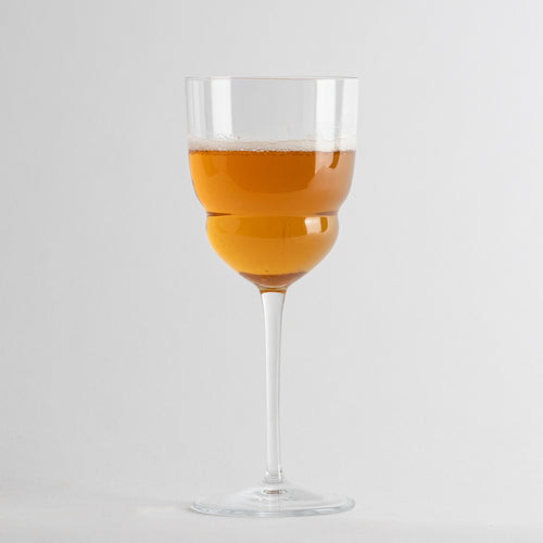 Transparentes Glas-Weinglas mit langem Stiel, gefüllt mit schaumigem orangefarbenem Getränk auf weißem Hintergrund