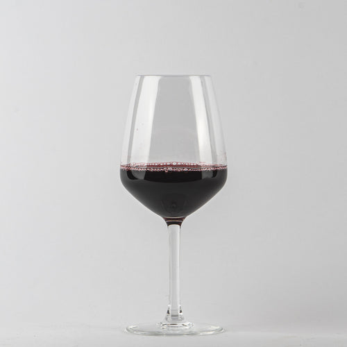 Transparent glass wine glass with red wine and bubbles on light grey background