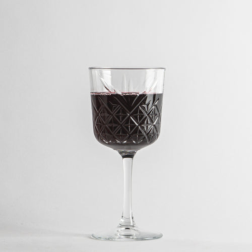 Transparentes Glas mit geometrischen Verzierungen, mit dunkelrotem Wein gefüllt, weißer Hintergrund.
