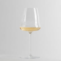 Transparent glass wine glass with long stem containing lightly sparkling white wine on grey background