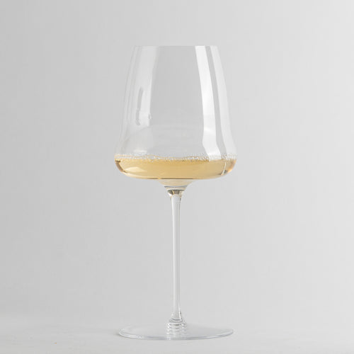 Calice di vetro trasparente con gambo lungo contenente vino bianco leggermente frizzante su sfondo grigio