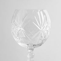 Rundes transparentes Glas-Weinglas mit floralen Gravuren und verziertem Stiel auf hellgrauem Hintergrund