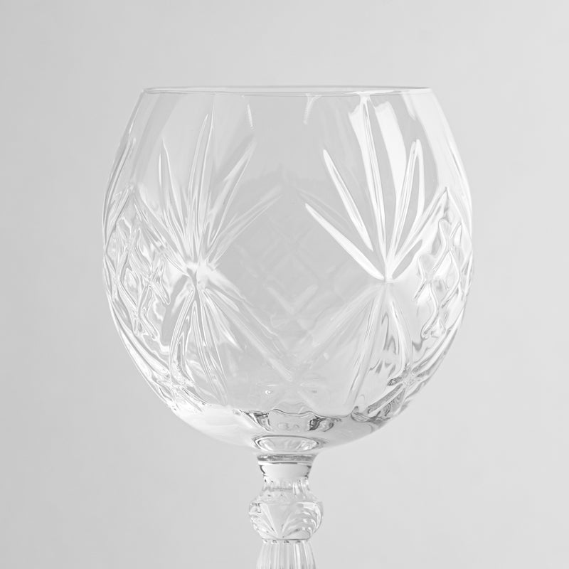 Rundes transparentes Glas-Weinglas mit floralen Gravuren und verziertem Stiel auf hellgrauem Hintergrund