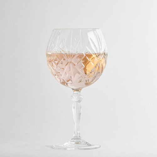 Transparentes Glas-Weinglas mit geometrischen Gravuren, gefüllt mit rosafarbenem Getränk und Zitronenscheibe, Hintergrund