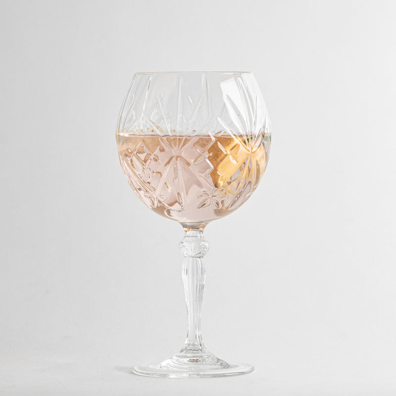 Transparentes Glas-Weinglas mit geometrischen Gravuren, gefüllt mit rosafarbenem Getränk und Zitronenscheibe, Hintergrund