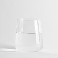 Transparante glazen beker met acqua halfvol op uniform witte achtergropd