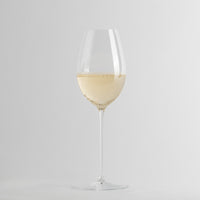 Transparant wijnglas met witte wijn en bellen op minimalistische lichtgrijze achtergrond