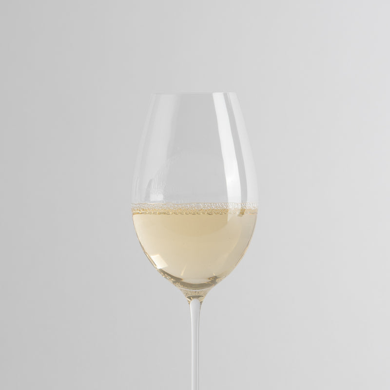 Transparante glazen wijnglas met lichte witte wijn en licht mousserend oppervlak op lichtgrijze achtergrond.