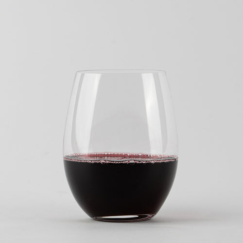 Transparent stemless tumbler with dark red wine on white background.