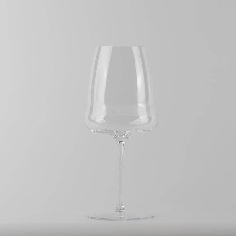 Calice trasparente in vetro con gambo lungo e base tonda, su sfondo grigio uniforme.