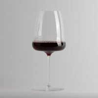 Calice trasparente in vetro con vino rosso all'interno su sfondo grigio chiaro.