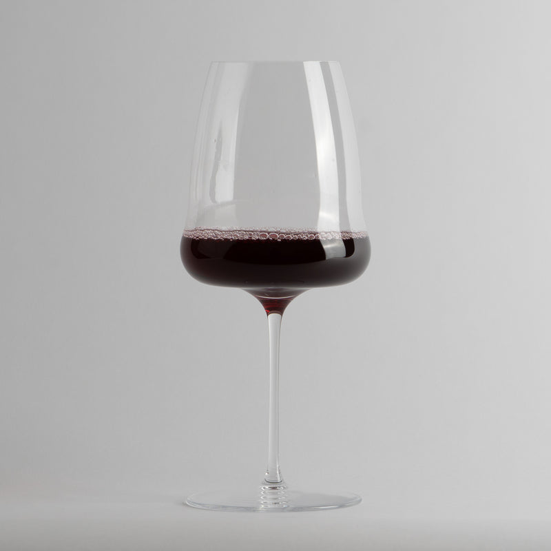 Calice trasparente in vetro con vino rosso all'interno su sfondo grigio chiaro.