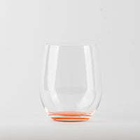 Verre transparent en verre avec base rouge sur fond blanc, sans liquide à l'intérieur.