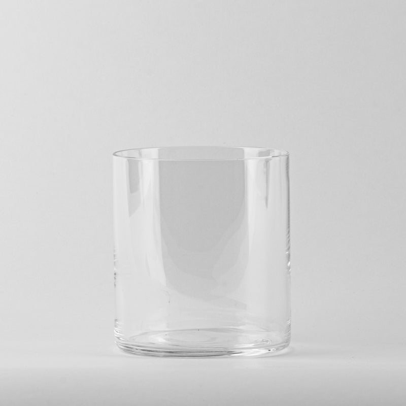 Vaso transparente de cristal liso y cilíndrico sin decoraciones sobre fondo gris claro.