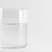 Vaso transparente cilíndrico de cristal con agua clara, fondo blanco uniforme.
