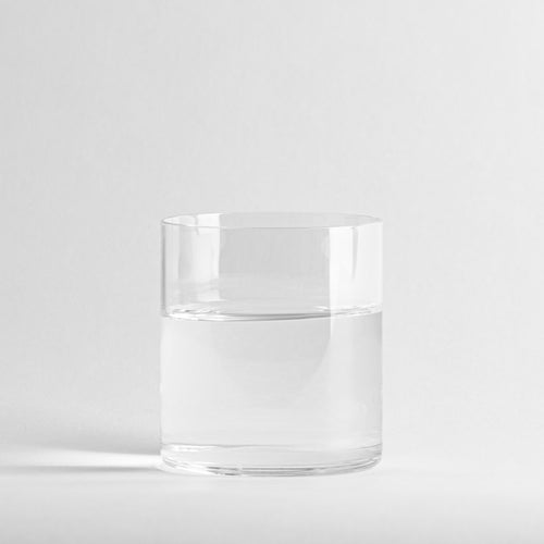 bicchiere trasparente cilindrico di vetro contenente acqua, su sfondo bianco uniforme